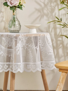 Detail of white floral lace tablecloth with scalloped edges on a round wooden table