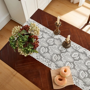 Detail of white lace table runner with floral patterns and scalloped edges on dark wood
