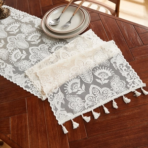 Elegant off-white lace table runner with floral patterns and tassels on wooden desk