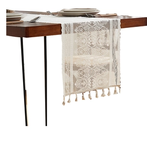 Elegant cream lace table runner with floral patterns and tassels on a wooden dining table
