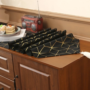 Nordic black and gold table runner with geometric lines and white tassels on a wooden cabinet