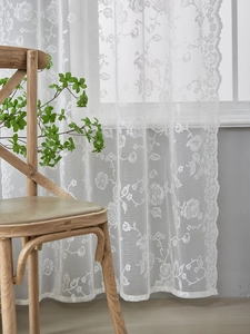 Detailed macro view of white floral lace curtains with intricate rose patterns and wavy edges