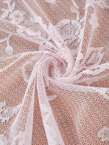 Detailed macro view of light pink French lace fabric with delicate floral pattern weave