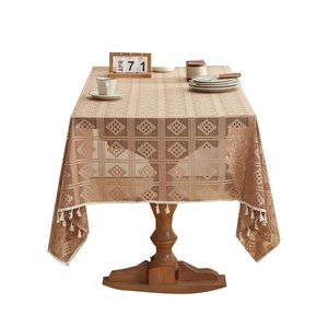 Beige hollow lace tablecloth with delicate white tassel edges on a wooden table