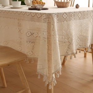Detailed view of beige crochet lace tablecloth with cotton tassels and boho pattern