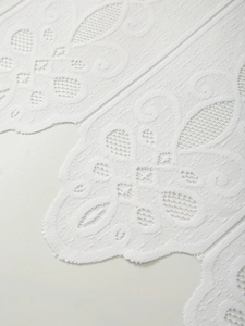 Close-up of white lace curtain showing intricate floral embroidery and mesh texture details