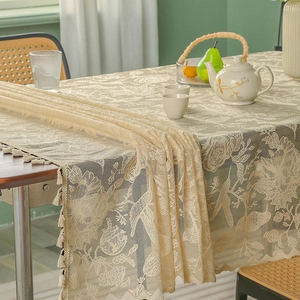 Elegant vintage beige lace tablecloth with floral patterns and tassels on a wooden table