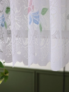 Close-up of white lace curtain with colorful floral prints and delicate wavy scalloped edges