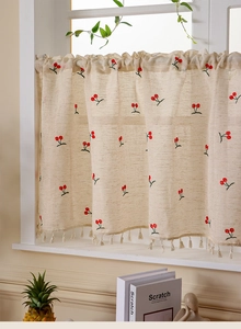 Close-up of beige linen cafe curtain with red cherry embroidery and tassel trim