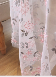 Close-up detail of white lace mesh tablecloth with pink floral and grey leaf embroidery