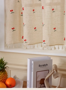 Detail of linen cafe curtain with embroidered cherry patterns and cotton tassel fringe