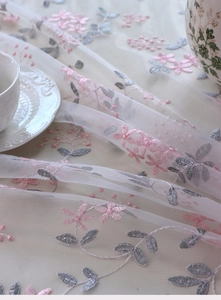 Detailed macro view of delicate pink floral embroidery on translucent beige lace mesh fabric