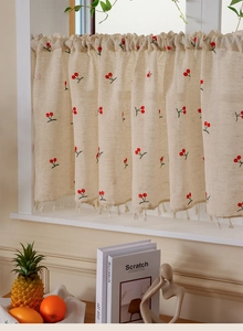 Detail of linen cafe curtain with cherry embroidery and beige tassel fringe on window