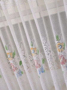 Detailed macro view of white lace curtain with delicate colorful floral print and mesh texture