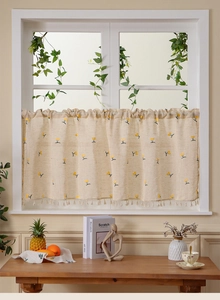 Detailed close-up of a linen cafe curtain with yellow floral print and white fringe trim