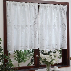 Detailed close-up of white lace cafe curtain with delicate floral embroidery on wood window