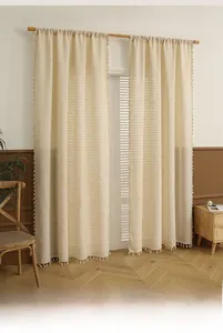 Close-up of beige linen door curtains with decorative white tassel trim for privacy