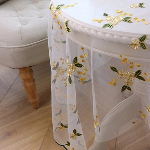 Lace embroidery tablecloth with yellow floral patterns on a white round dining table