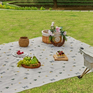 Outdoor folding floral picnic mat on green grass with picnic basket and flowers