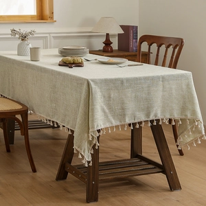 Linen textured green tablecloth with cream fringe tassels on a wooden dining table