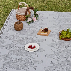 Outdoor grey picnic mat with tulip jacquard and lace edges on green grass lawn
