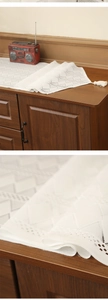 Detail of white hollow-out lace table runner with tassels on a dark wood cabinet