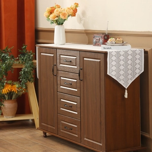 White lace table runner with geometric patterns and tassels on a wooden cabinet