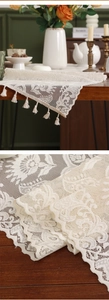 Detailed close-up of cream white lace table runner with floral hollow patterns and tassels