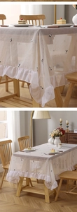 Detail of off-white lace tablecloth featuring cat embroidery and ruffled edges for dining