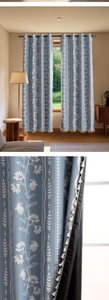 Close-up of blue floral blackout curtain with white pom-poms and metal eyelets
