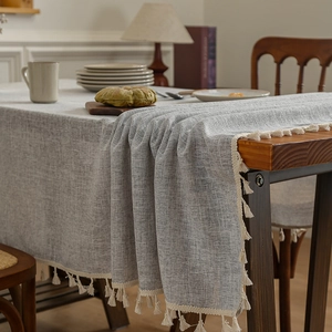 Linen texture grey tablecloth with beige tassels on a wooden dining table