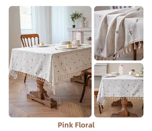 Dettaglio del ricamo floreale rosa e frange su una tovaglia di lino con trama rustica