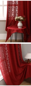 Close-up of red lace hollow curtains with white floral patterns and draped texture