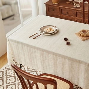 Minimalist cream linen tablecloth with vertical stripes and tassel fringe on wooden table