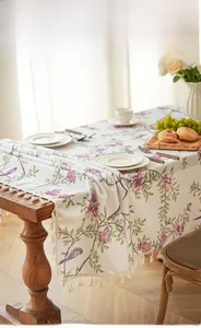 Detail eines Tischläufers mit Blumen- und Vogelprint sowie Quasten auf dem Holztisch