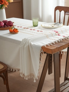 Close-up of geometric embroidery and tassel fringe on a cream cotton linen tablecloth