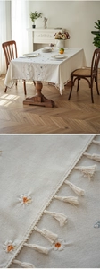 Detail of linen tablecloth featuring daisy embroidery and decorative fringe tassels