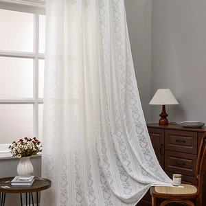 White lace sheer curtain with grey floral pattern in a cozy sunlit bedroom