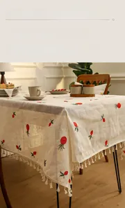 Detail of linen tablecloth with red fruit embroidery and delicate fringe edges