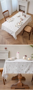 Detail of cream rectangular tablecloth with pink floral embroidery and cotton ball tassels