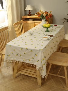 Detail of yellow floral embroidery and cream fringe tassels on a cotton linen tablecloth