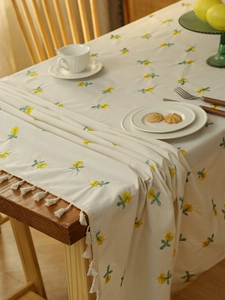Detailed view of beige cotton linen tablecloth with yellow floral embroidery and white tassels