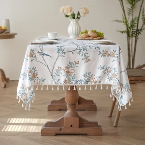 Floral and bird print tablecloth with fringe tassels on a wooden dining table