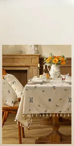 Close-up of retro floral embroidery on beige linen tablecloth with white pom-pom fringe