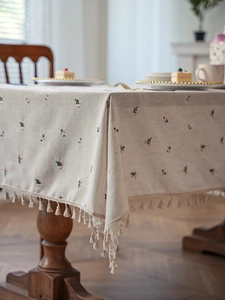 Detailed close-up of beige linen texture tablecloth with pink floral embroidery and fringe