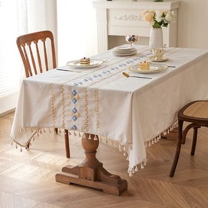 Waterproof off-white tablecloth with geometric embroidery and fringe on wooden table