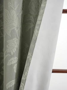 Detail of grey-green jacquard fabric showing plant leaf texture and thick white blackout lining