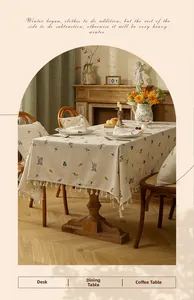 Detail view of cream linen tablecloth with floral embroidery and decorative pom-pom fringe