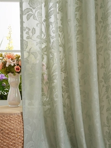 Detail eines hellgrünen halbtransparenten Spitzenvorhangs mit feinen Blumenmustern