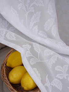 Detailaufnahme der weißen Spitzengardine mit zarten Blattmustern und lichtdurchlässiger Textur